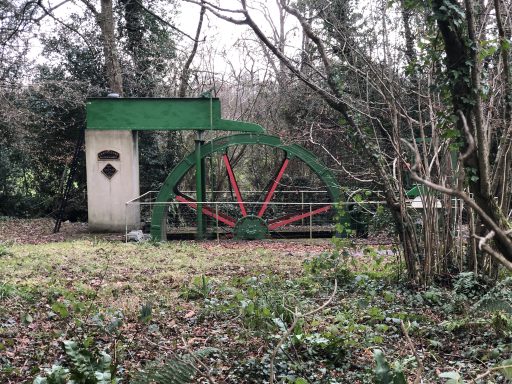 A water wheel with red spokes and a green rim in a wooded area