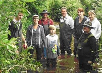 A group of volunteers in waders standing knee deep in river water.