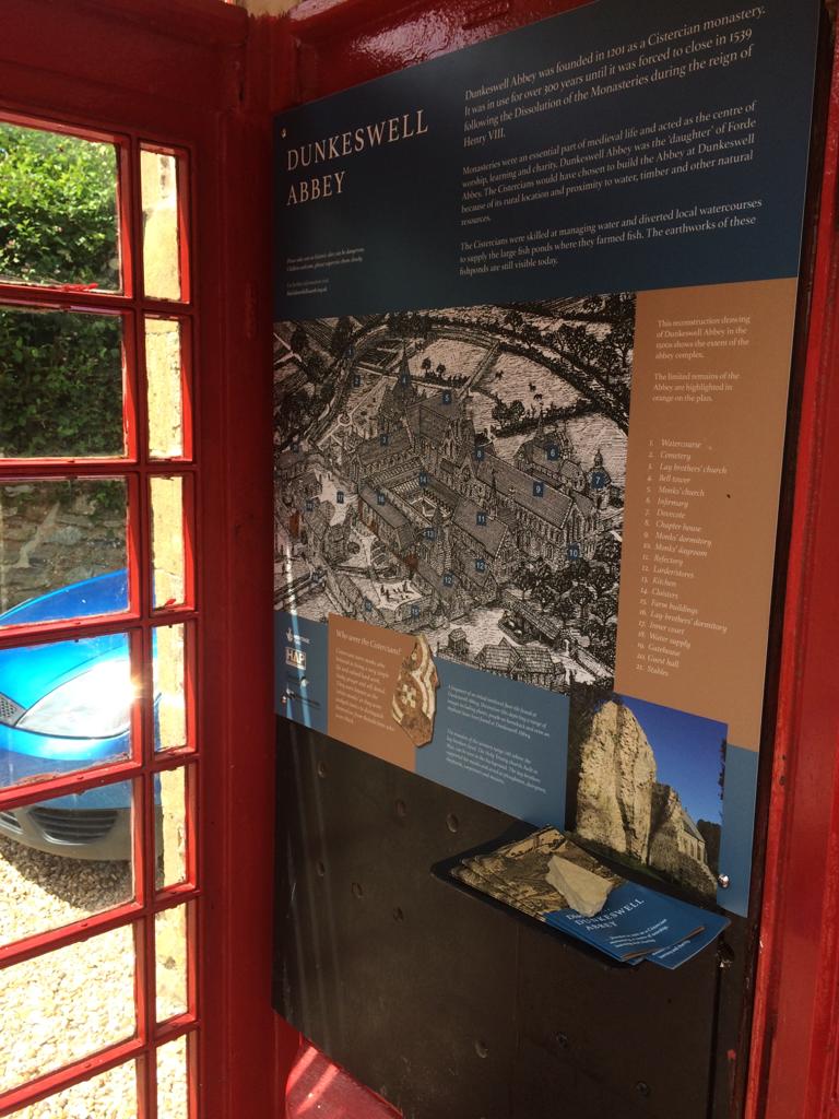 An interpretation board inside a telephone box showing a line drawing of how Dunkeswell Abbey would have looked.