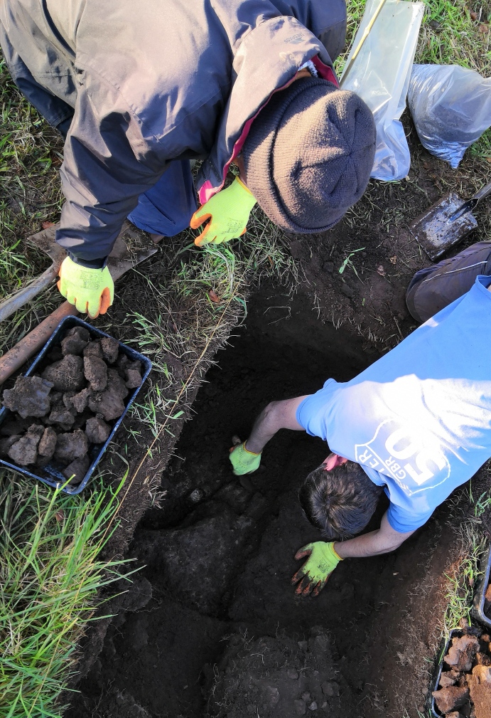 Volunteers look into a deep neatly-cut trench in the ground.