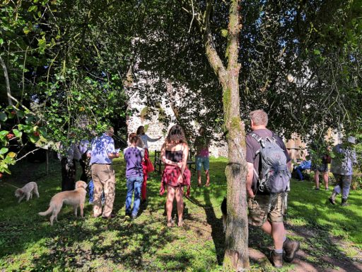 A group of people stand amongst trees in front of the ruined walls of Dunkeswell Abbey