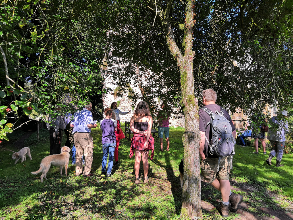 A group of people stand amongst trees in front of the ruined walls of Dunkeswell Abbey