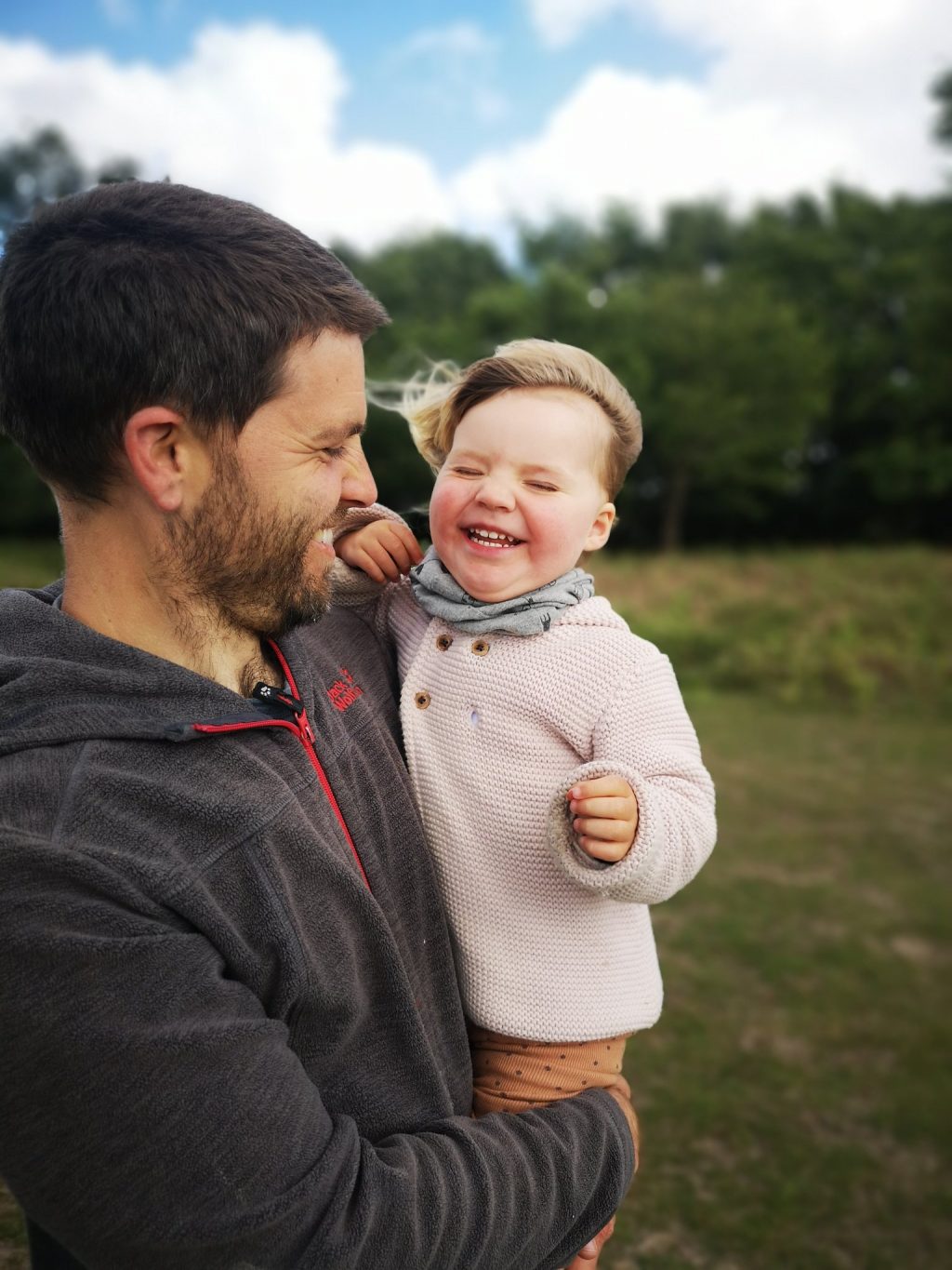 A man holding a small child as they smile and the wind blows through their hair.