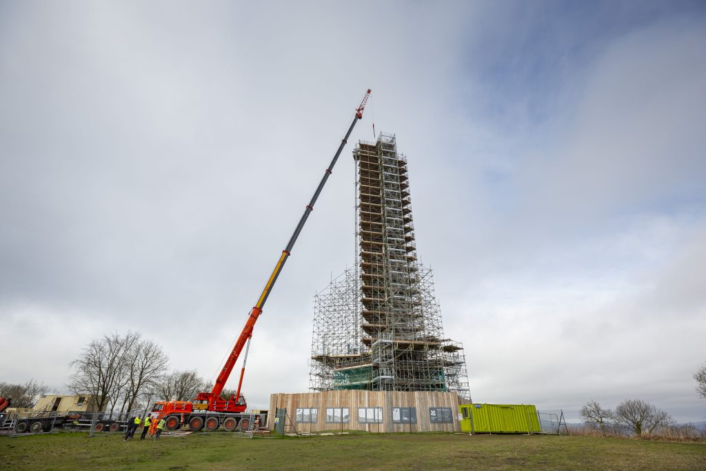 Wellington Monument covered with scaffolding, with a tall crane beside it lifing the large capstone into place