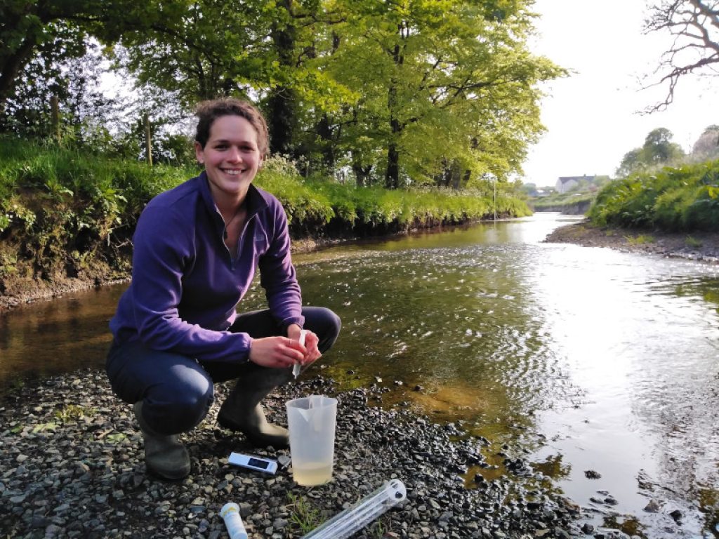 woman knelt beside river Culm sampling