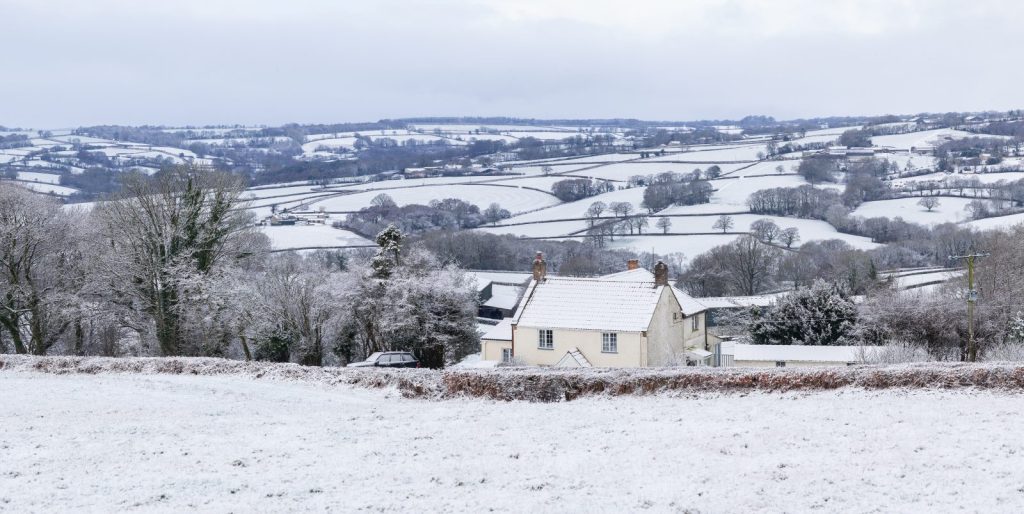 A farm house with a backdrop of fields and hedges in the snow