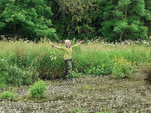 a woman with grey hair stood in a wooded area holding a tree cutting