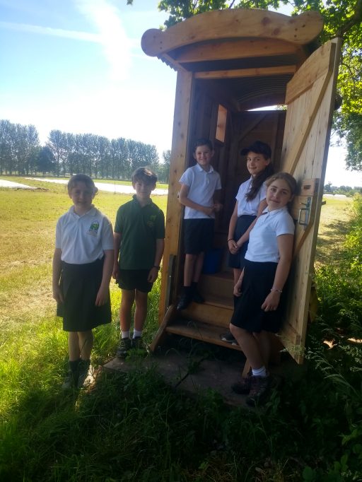 five children in school uniform looking at there new compost toilet