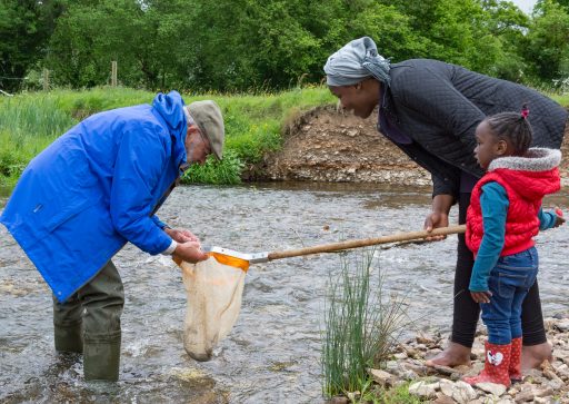 two adults and one young child fishing in a shallow river with a fishing net