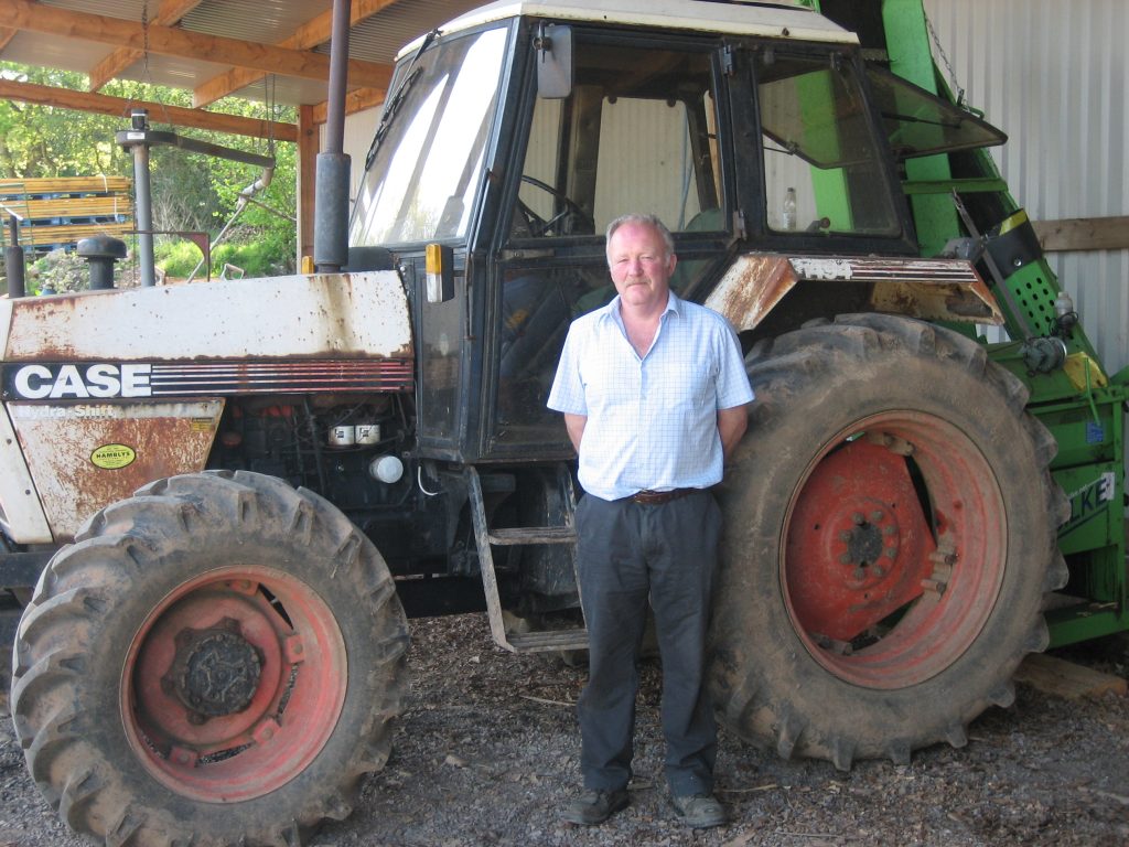 John Greenshields standing in front of a tractor in a barn