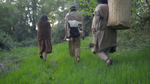 People dressed in costumes, carrying baskets walking through woodland