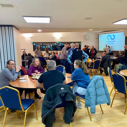 Groups of people have conversation around tables with a presentation screen in the background