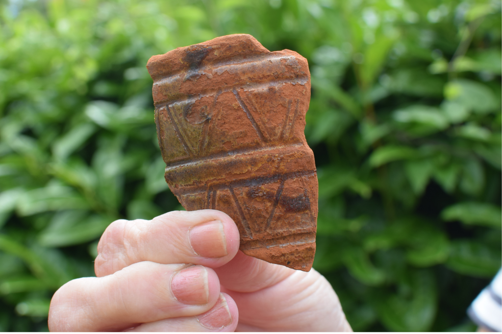 A hand holding up a broken piece of clay pot