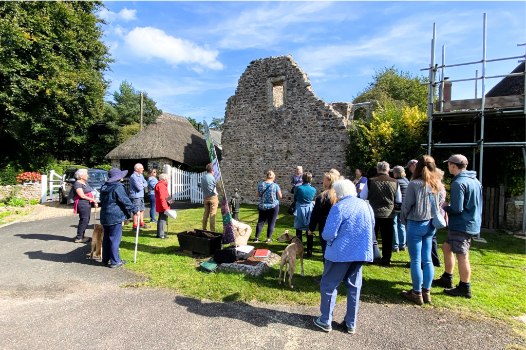 A group of people standing looking at the remains of Dunkeswell Abbey