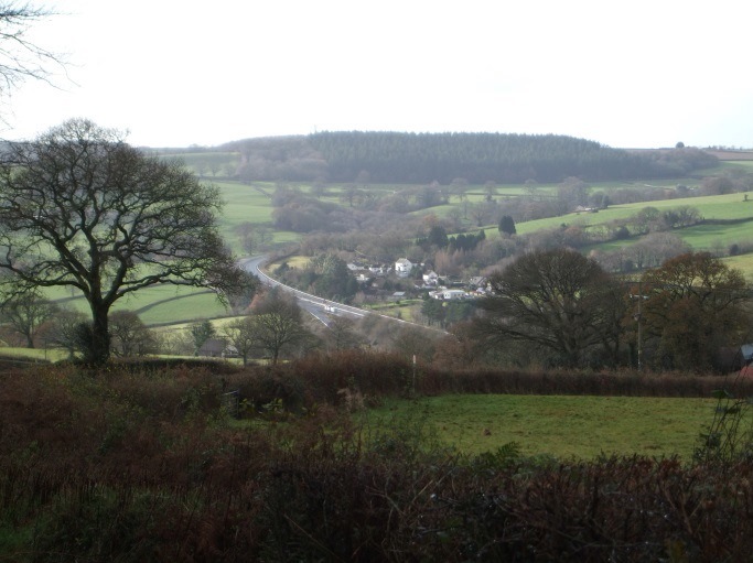 A road running through a valley of green fields and trees.