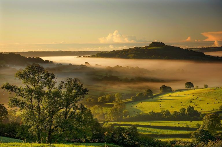 Dumpdon Hill surrounded by morning mist in the valley with shadows across fields.