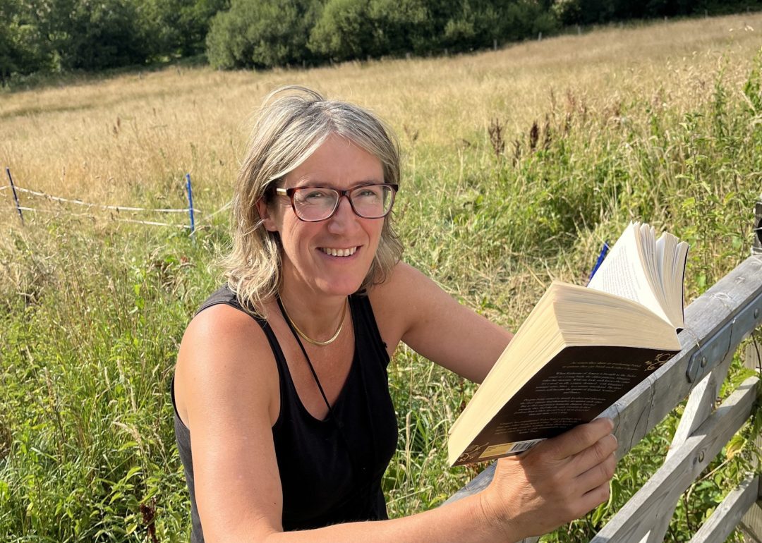 Vanessa Da Haan reading her book whilst leaning on a field gate